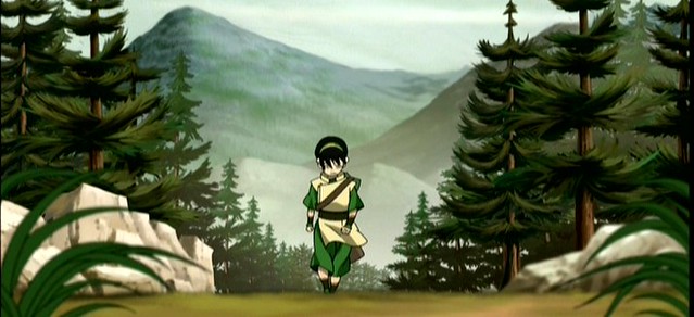 A landscape picture of a forest with mountains in the background. Toph's small figure in the middle coming up the trail still seems very bold and powerful. She is solitary, but in stride and determined. 