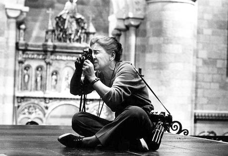 Eve Arnold sits cross-legged on the floor looking through a camera lens