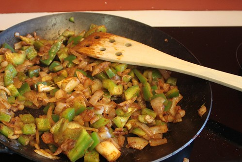 Photo of onions and peppers sauteing in a frying pan on a cook top.