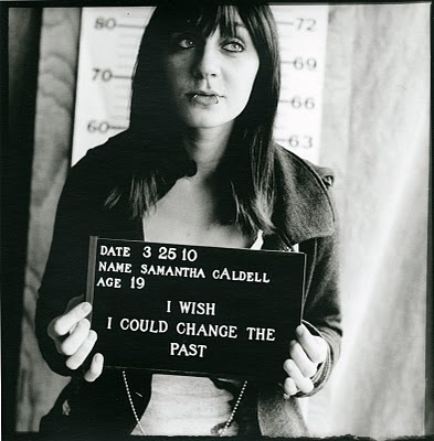 Black and white mugshot-style photo of a white woman aged 19. The placard she's holding says I wish I could change the past
