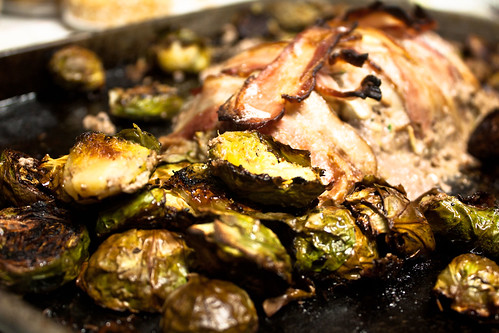 Photo of Brussels sprouts and meatloaf covered in bacon on a cookie sheet ready to serve.