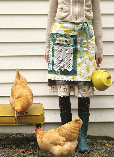 A white woman from the neck down, holding a watering can and wearing an apron. She is surrounded by chickens. From dottieangel.blogspot,com