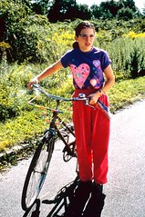 Girl in purple shirt and pink sweatpants standing next to a bicycle.