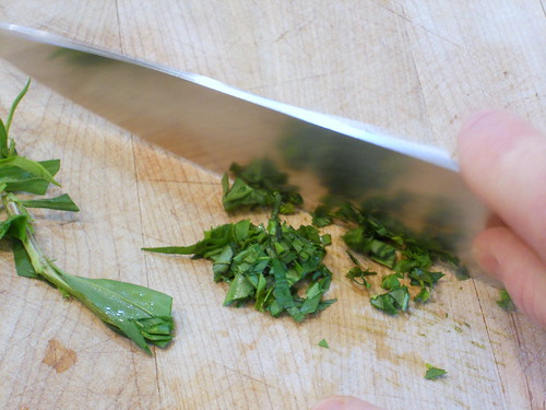 Chef's knife cutting up fresh tarragon on a wooden board.