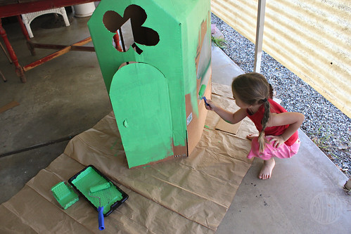 child painting cardboard house with green paint 