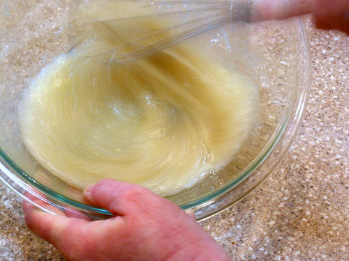 Hand mixing with a whisk, egg whites with sugar in a clear mixing bowl.