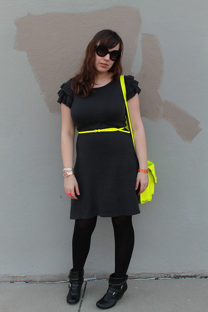Neon and charcoal outfit: black booties, black tights, knit charcoal dress with ruffled shoulders, neon belt, neon satchel, Prada baroque sunglasses, rose gold watch, two-tone diamond watch