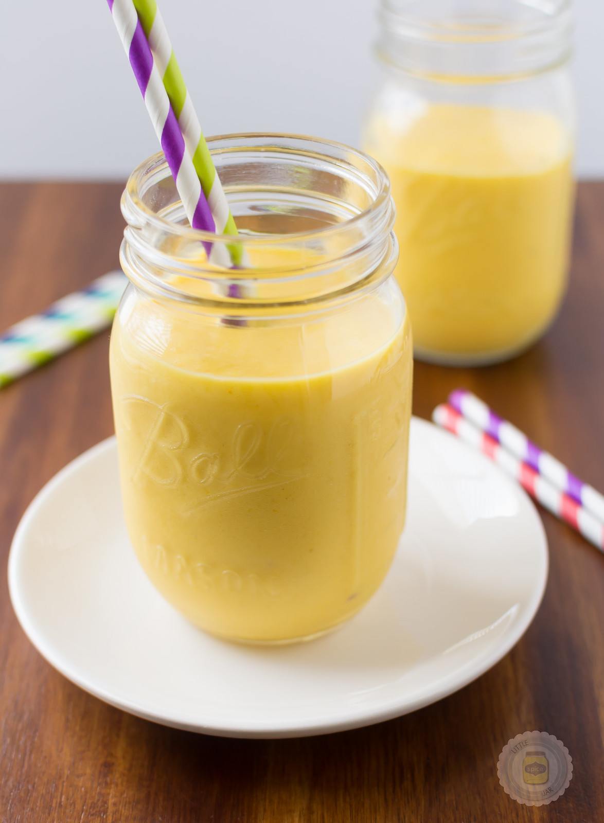 smoothie in mason jar with two colorful straws on white plate