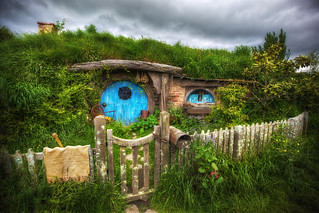 Hobbit hole set from Lord of the Rings film series, color photograph of round blue door set in grassy hill behind picket fence