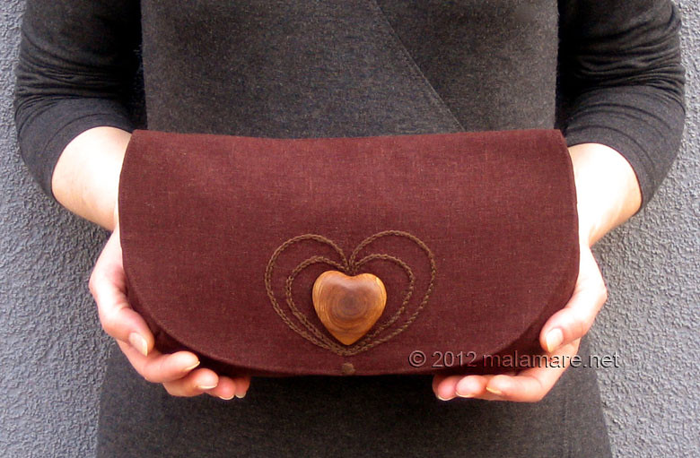 brown linen fabric clutch bag with olive wood heart and hand embroidered heart motif in hands