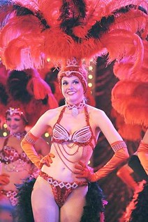 the protagonist of bunheads stands straight up in an all red showgirls outfit with feathers on her head