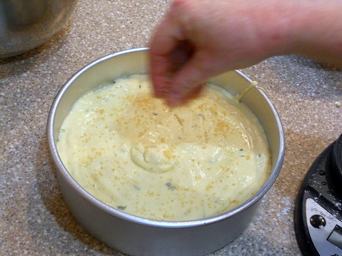 Batter for lemon tarragon olive oil cake poured into a round cake tin and sprinkling sugar over the top before baking.