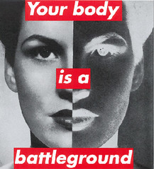 A print of a white woman's face divided in half, with one half portrayed in the negative. Red and white letters read Your Body is a Battleground
