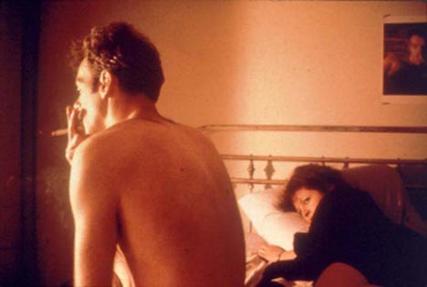 photo of Nan Goldin in bed. A man is sitting up smoking a cigarette.