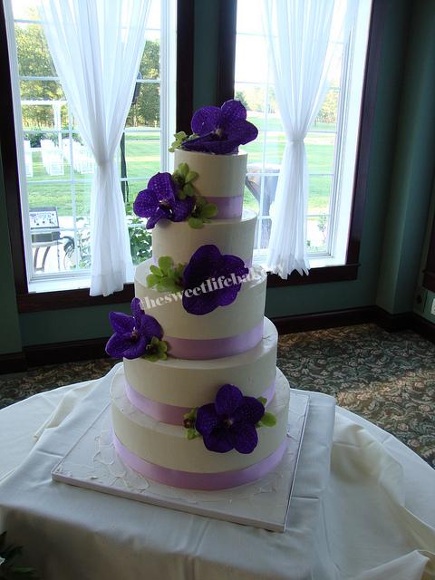 A simple 5 tier white wedding cake is accented with large purple orchids and