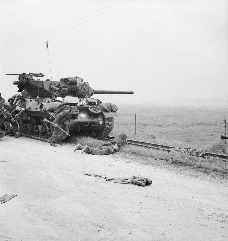 Troops take shelter near an M10 Wolverine tank destroyer.
