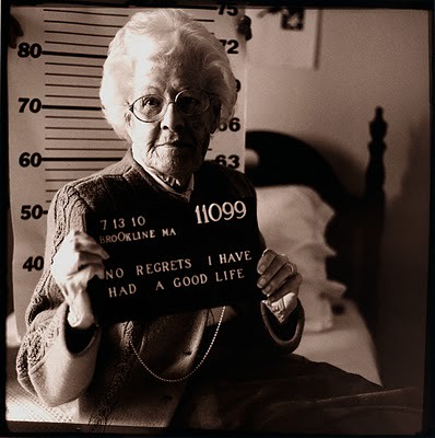 Black and white mugshot-style photo of an older white woman. Placard reads No regrets I have had a good life