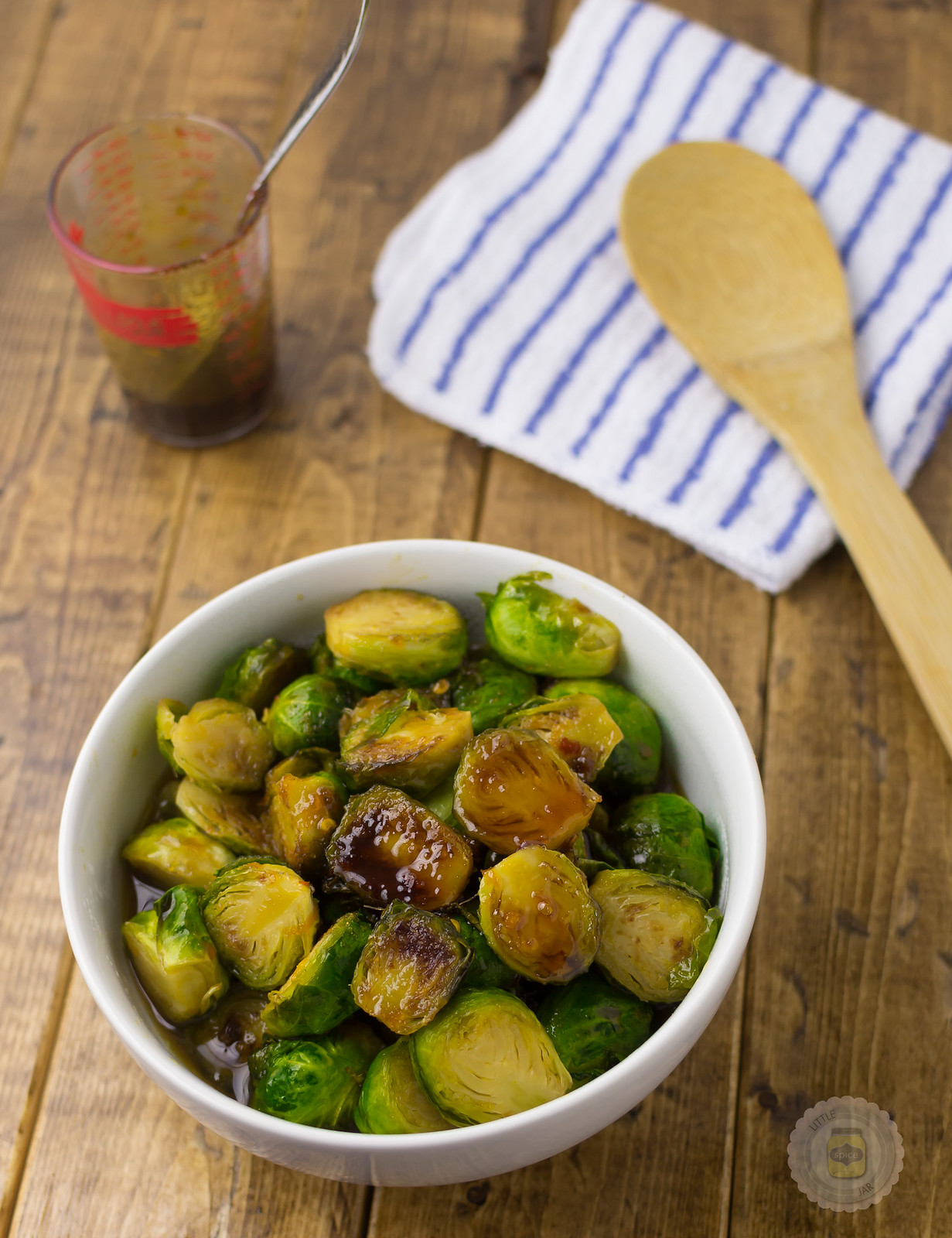 prepared soy glazed Brussel sprouts in a white bowl with wooden spoon and towel in the back