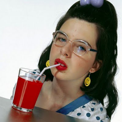 Girl wearing glasses and red lipstick sipping from a straw in a glass filled with bright red liquid