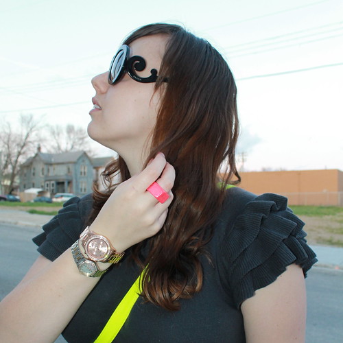 Neon and charcoal outfit: black booties, black tights, knit charcoal dress with ruffled shoulders, neon belt, neon satchel, Prada baroque sunglasses, rose gold watch, two-tone diamond watch