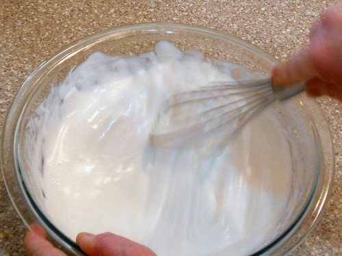 Clear mixing bowl with egg whites being whisked and volume has increased, whites are taking on a shiny appearance.