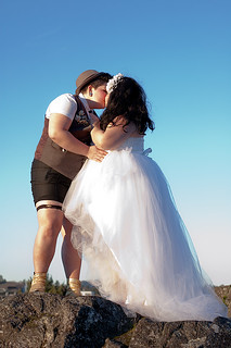 a person in tux shorts, hat, and bowtie kissing a bride