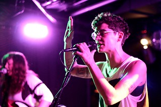 JD Samson performing with MEN live in Vancouver, Canada. The light is purple and her arm is at a 90 degree angle with her hand in the air