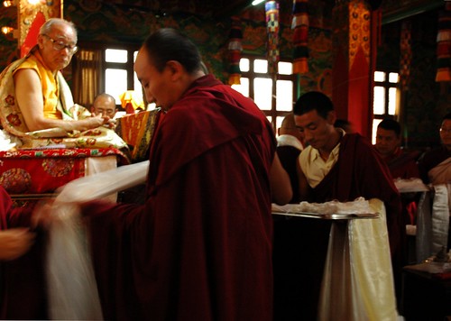 A Tibetan lama prepares a khata during a mandala offer to His Holiness Jigdal Dagchen Sakya, wearing traditional silk garments on his throne, Sakya Lamdre, Tharlam Monastery of Tibetan Buddhism, Boudhanath, Kathmandu, Nepal by Wonderlane