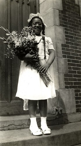 a black and white photo of Audre Lorde in the early 1940s, as a Roman Catholic schoolgirl, dressed for her First Communion.