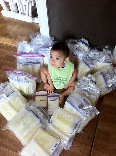 Baby sitting on the floor surrounded by bags of donor milk