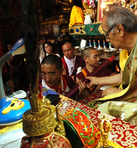 His Holiness Jigdal Dagchen Sakya recieves a rolled up Thangka from a monk during mandala offering, more monks and students wait in line, lama's table fine objects, silks, Sakya Lamdre, Tharlam Monastery of Tibetan Buddhism, Boudha, Kathmandu, Nepal by Wonderlane