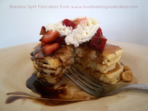 Banana Split Pancakes stacked on plate with whipped cream, strawberries and chocolate syrup close up with fork.