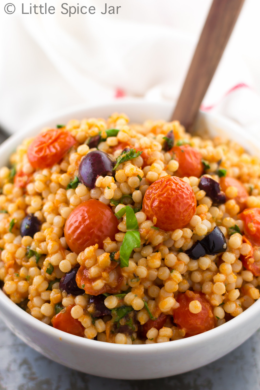 mediterranean pearl couscous salad with roasted cherry tomatoes and Kalamata olives showing in white bowl