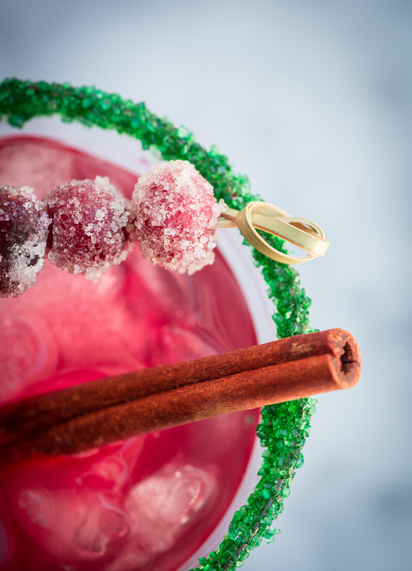 red cranberry margaritas in glasses with green sugar rim cinnamon sticks sugar covered cranberry skewers