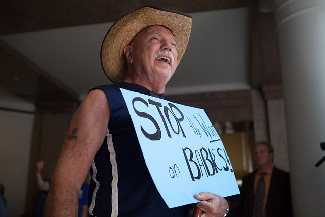 A man in a cowboy hat holds a sign that reads "stop the war on babies"