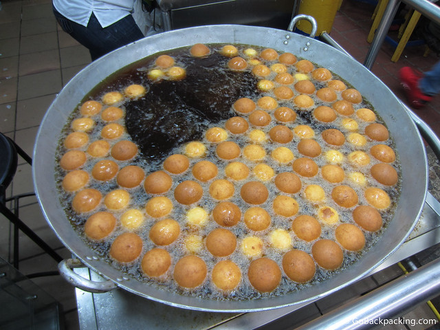 Buñuelos being deep fried in a vat of oil