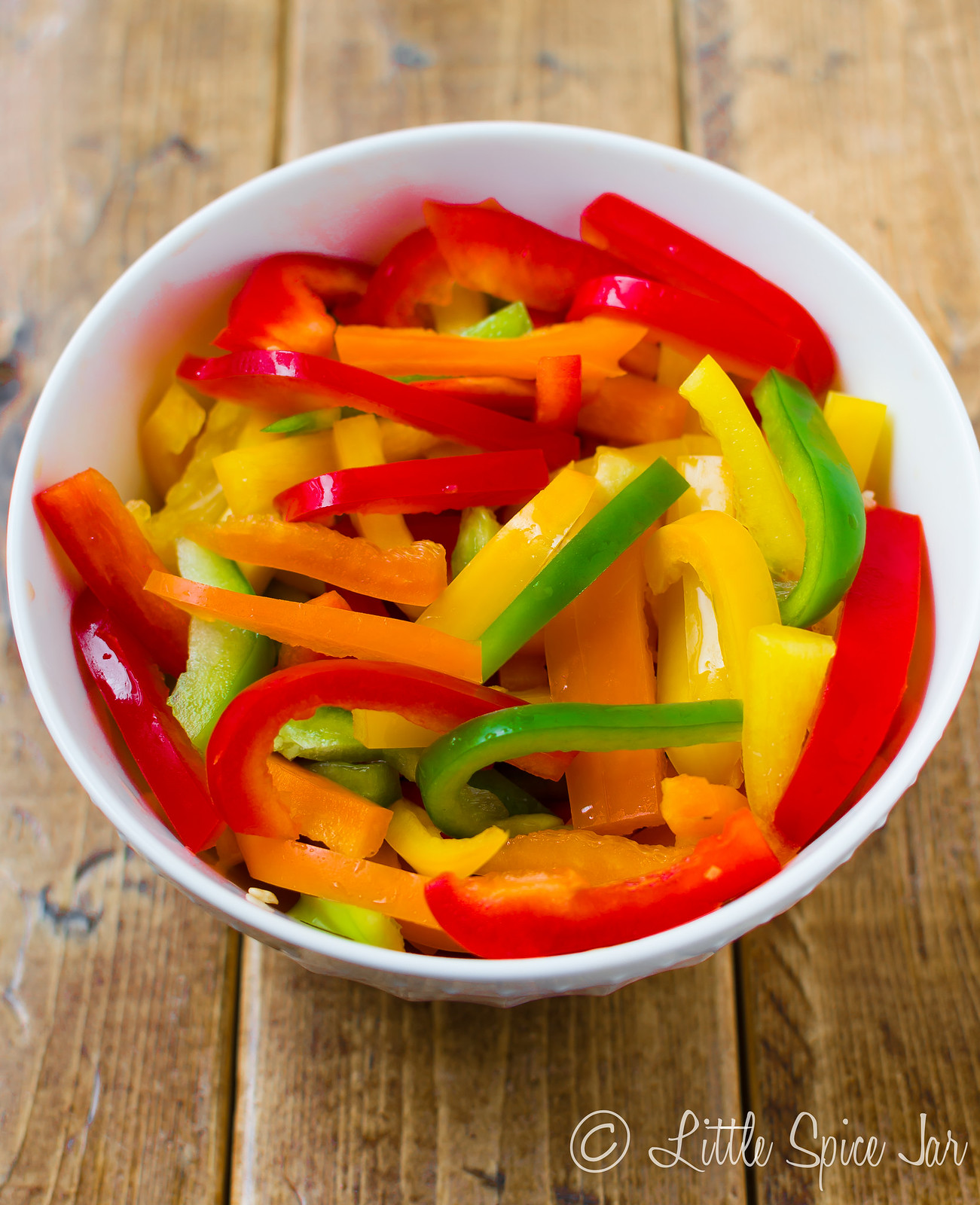 multi colored bell peppers in strips in white bowl on wood surface
