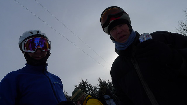 Upward, waist up view of 2 people wearing helmets and ski goggles, standing next to each other