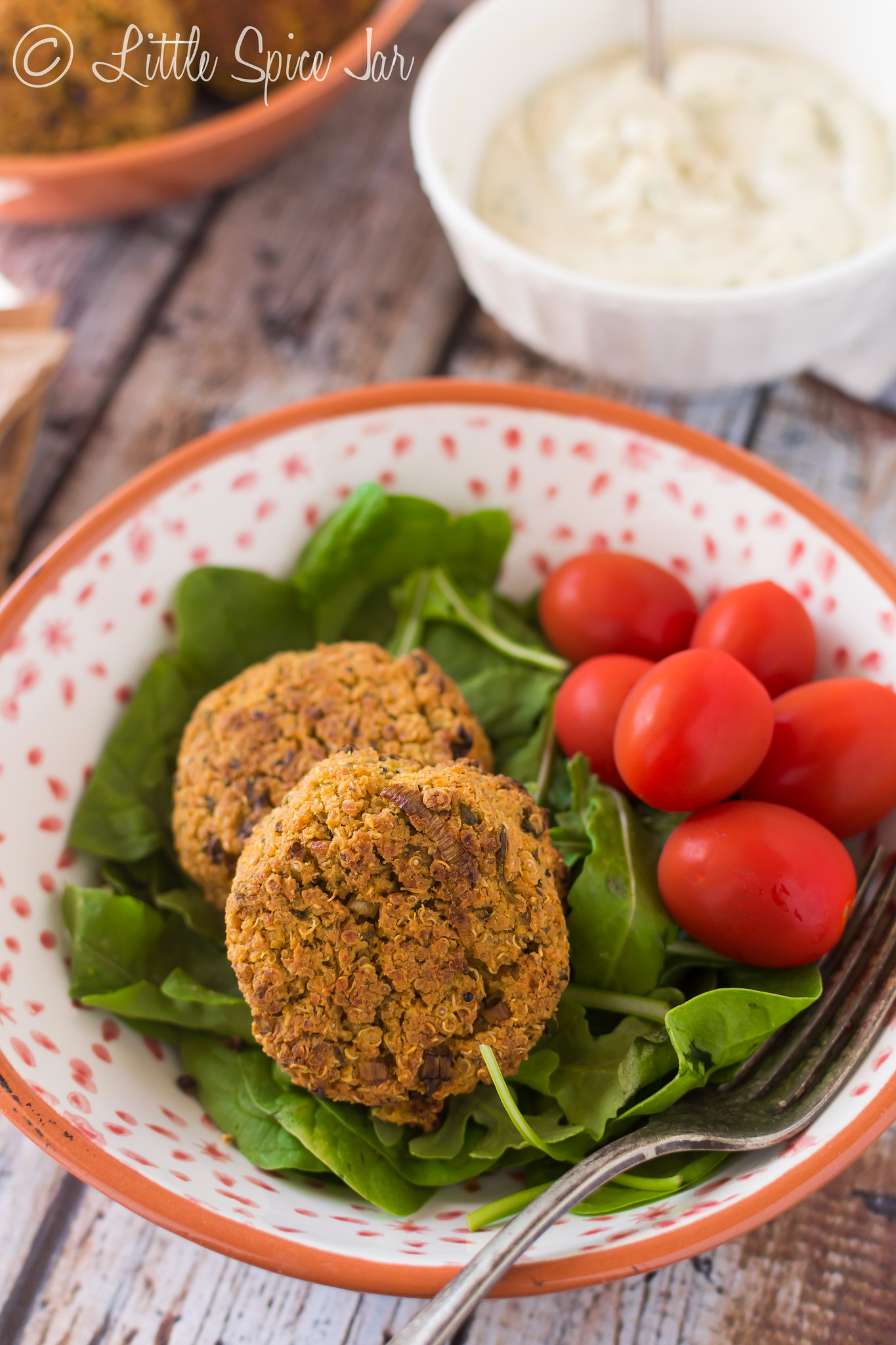 baked quinoa falafel on baby spinach with tomatoes in bowl