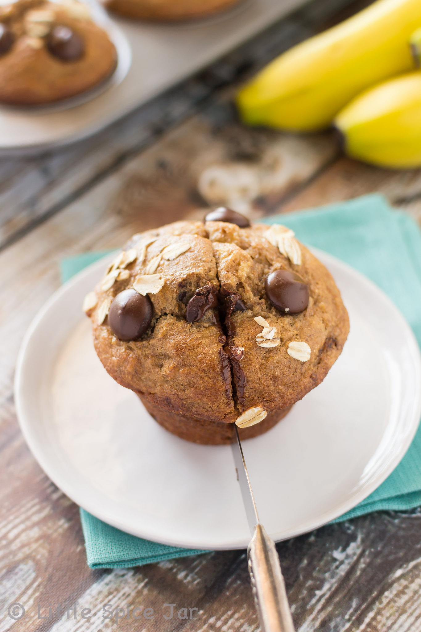 chocolate chip muffin slicing with knife on white plate