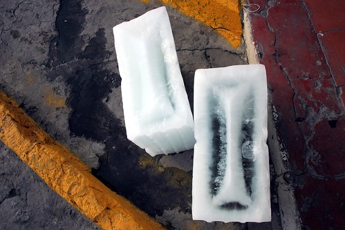 Art comes in pieces: 2 blocks of ice melting on the street, string, wet concrete, rough and smooth, lines, orange, red, gray, white, Mazatlan, Mexico by Wonderlane