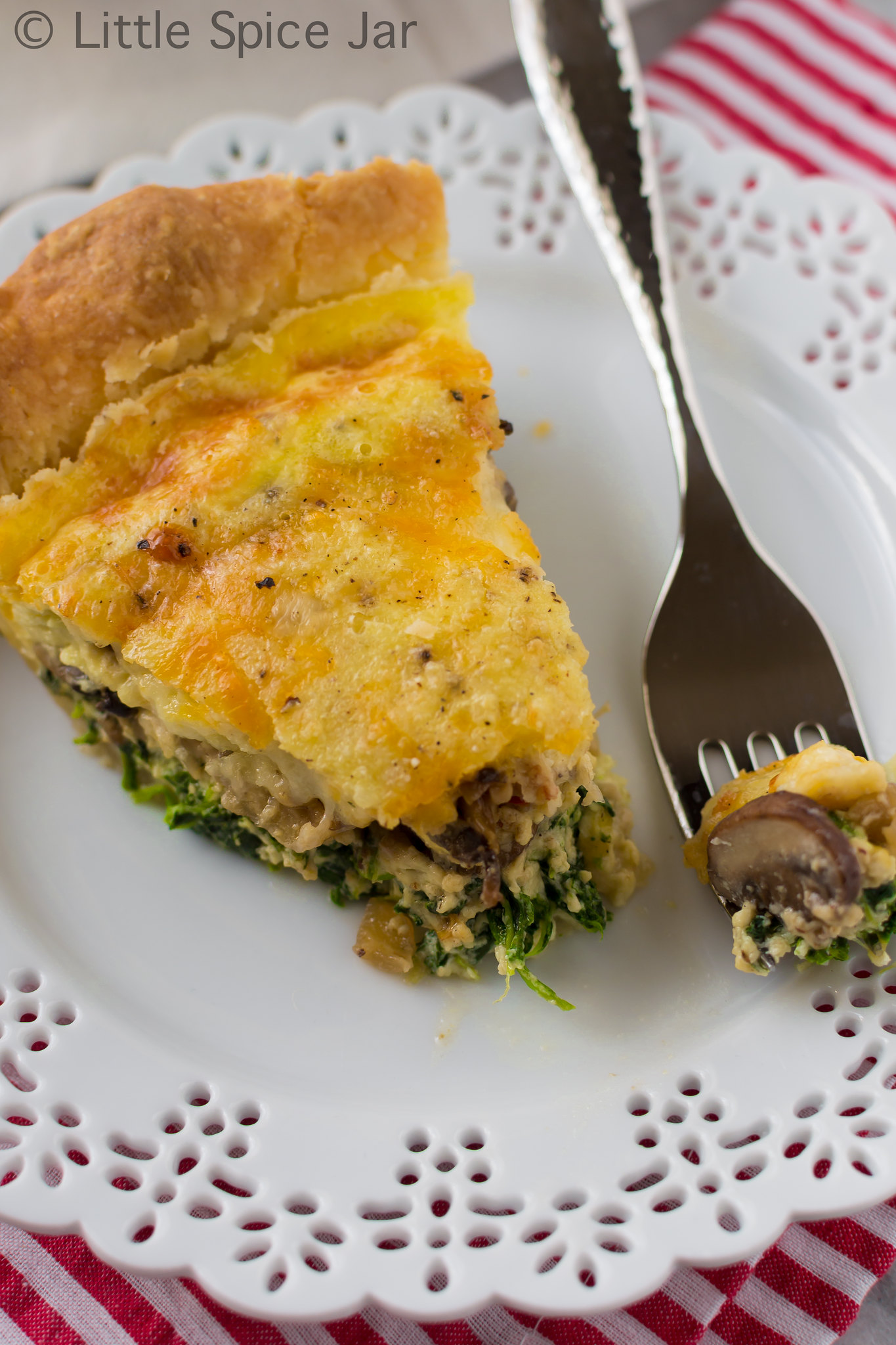 spinach mushroom quiche on a doily plate with fork