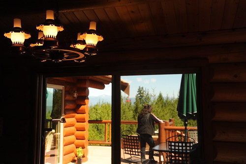 A neighbour standing on the deck taking in the view, wagon wheel lamp, patio furniture, through the sliding glass doors at Auntie's log cabin, Alderbrook Golf Course, Union, Washington, USA by Wonderlane