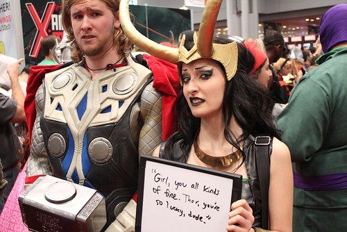 A cosplayer team dressed up as Thor and Jane Foster hold a sign that says, "Girl you all kinds of fine. Thor, you're a lucky dude."