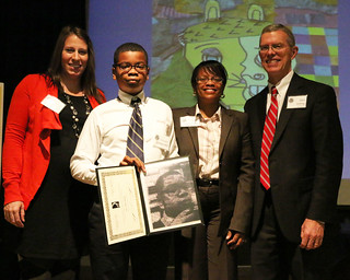 Chistopher Gilmer-Hill displays his Art From the Heart photograph with Middle School Art Teacher Sarah Kitchen (Left), his moter Dr. Holly Gilmer-Hill and Headmaster Glen Shilling