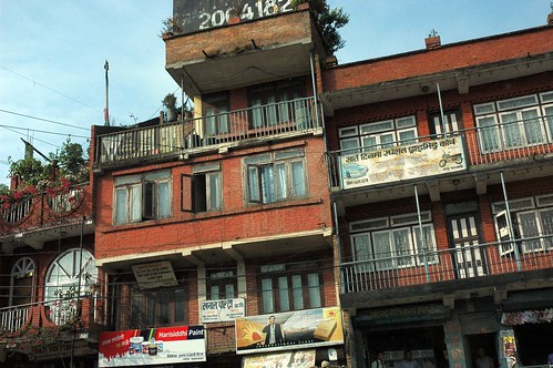 2064182 rugged Nepalese brick apartments, flowers, open windows, stores, magazines on display, banner advertising, Harisiddhi Paint, Kathmandu, Nepal by Wonderlane
