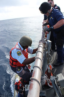 SOUTH PACIFIC- Lt. Joseph Anthony, U.S. Coast Guard Law Enforcement Detachment officer-in-charge, right, watches  Republic of Nauru Police Officer Falzon Laan climb down the accommodation ladder of the Arleigh Burke-class guided missile destroyer USS Kidd (DDG 100) to embark its rigid-hull inflatable boat to conduct a boarding of a fishing  vessel within Nauru's economic exclusive zone in support of the Oceania Maritime Security Initiative (OMSI). OMSI is a Secretary of Defense program that leverages Department of Defense assets transiting the region to increase the U.S. Coast Guard's maritime domain awareness, ultimately supporting its maritime law enforcement operations in Oceania. (U.S. Navy photo by Logistics Specialist 2nd Class Karolina Brooks)