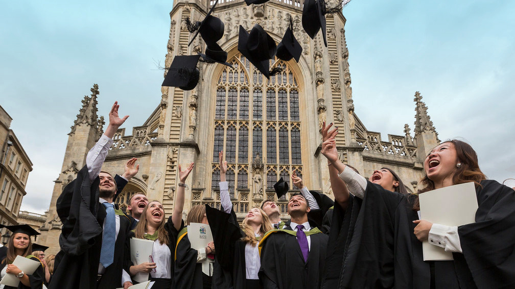 新毕业的学生穿着长袍，把他们的学位帽扔在教堂外