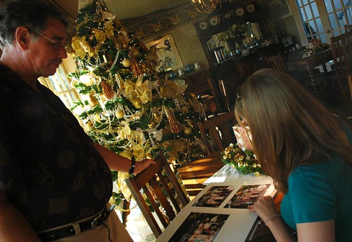 Ever thoughtful, co-owner Terry Baldwin watches bride-to-be Jessie look through wedding albums for ideas, under a yellow and gold Christmas tree, Mill Rose Inn, Half Moon Bay, California, USA by Wonderlane