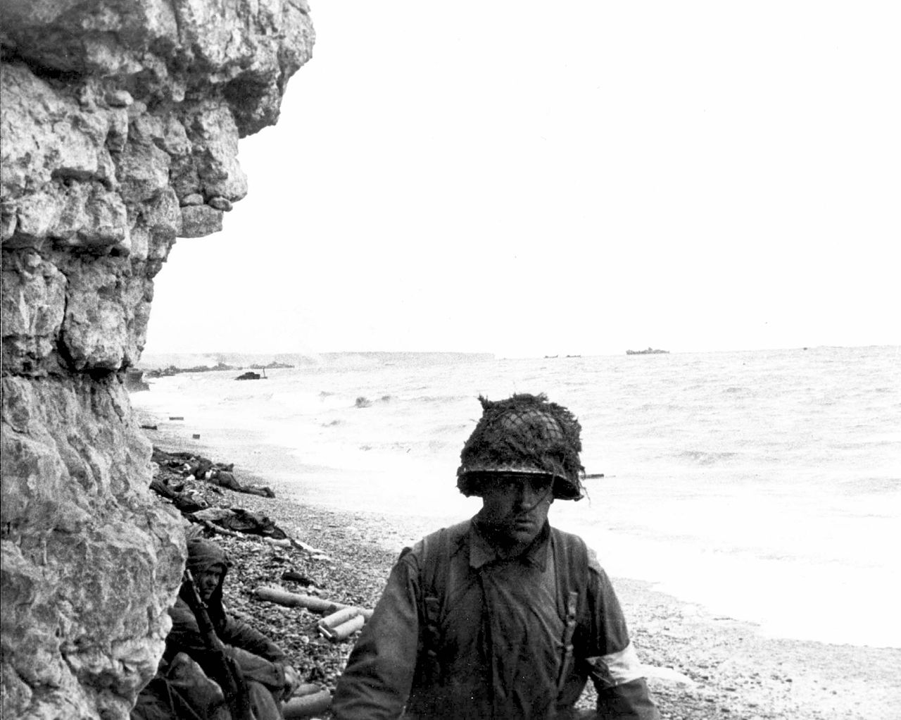 A medic of the 3d Bn., 16th Inf. Regt., 1st U.S. Inf. Div., moves along a narrow strip of Omaha Beach administering first aid to men wounded in the landing.